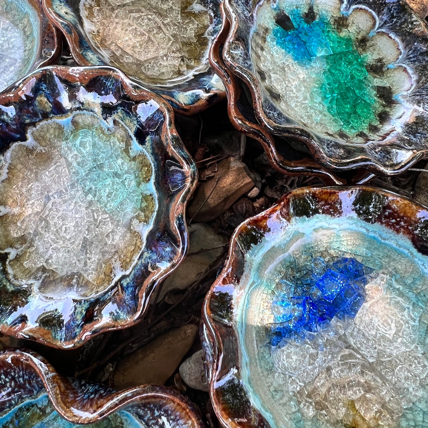 round blues and browns crackled glass little dish displayed with more round and hearts on a bed of leaves ad rocks