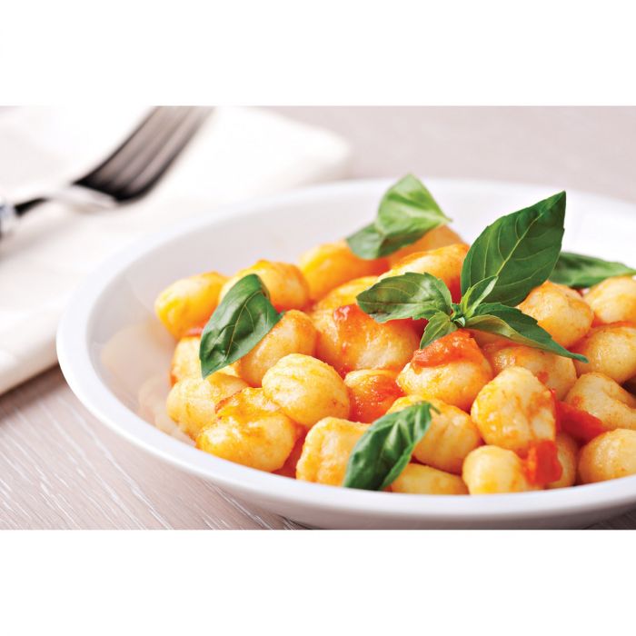 a bowl of gnocchi displayed on a table with a napkin and fork with a mostly white background