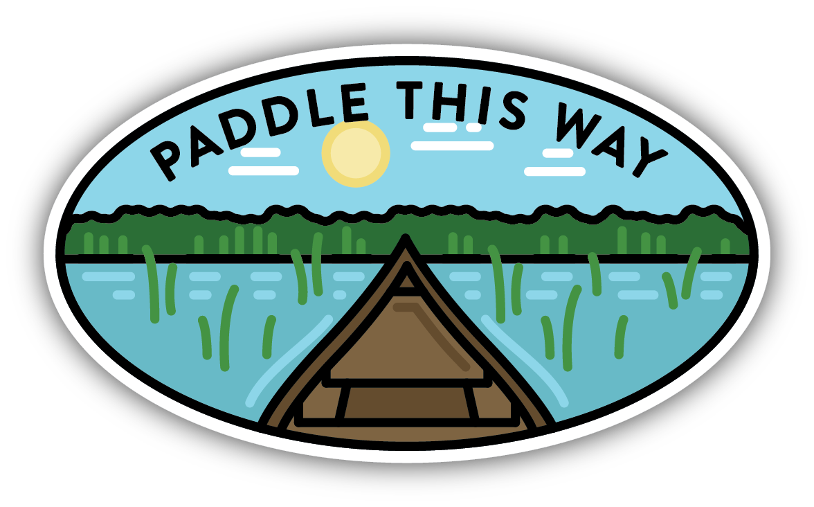 sticker on white background. oval sticker has graphic of river scene with trees, grasses, and sun in background and front end of canoe in foreground. "paddle this way" is written along the top.