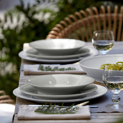 side view of table with grey dishes,, folded grey napkins with sprigs of greenery, wine glasses, and a serving bowl.
