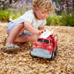 a young boy playing with the fire truck in wood chips outside