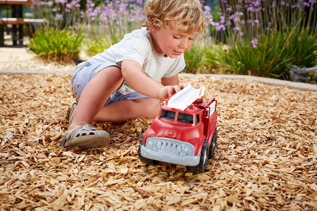 a young boy playing with the fire truck in wood chips outside
