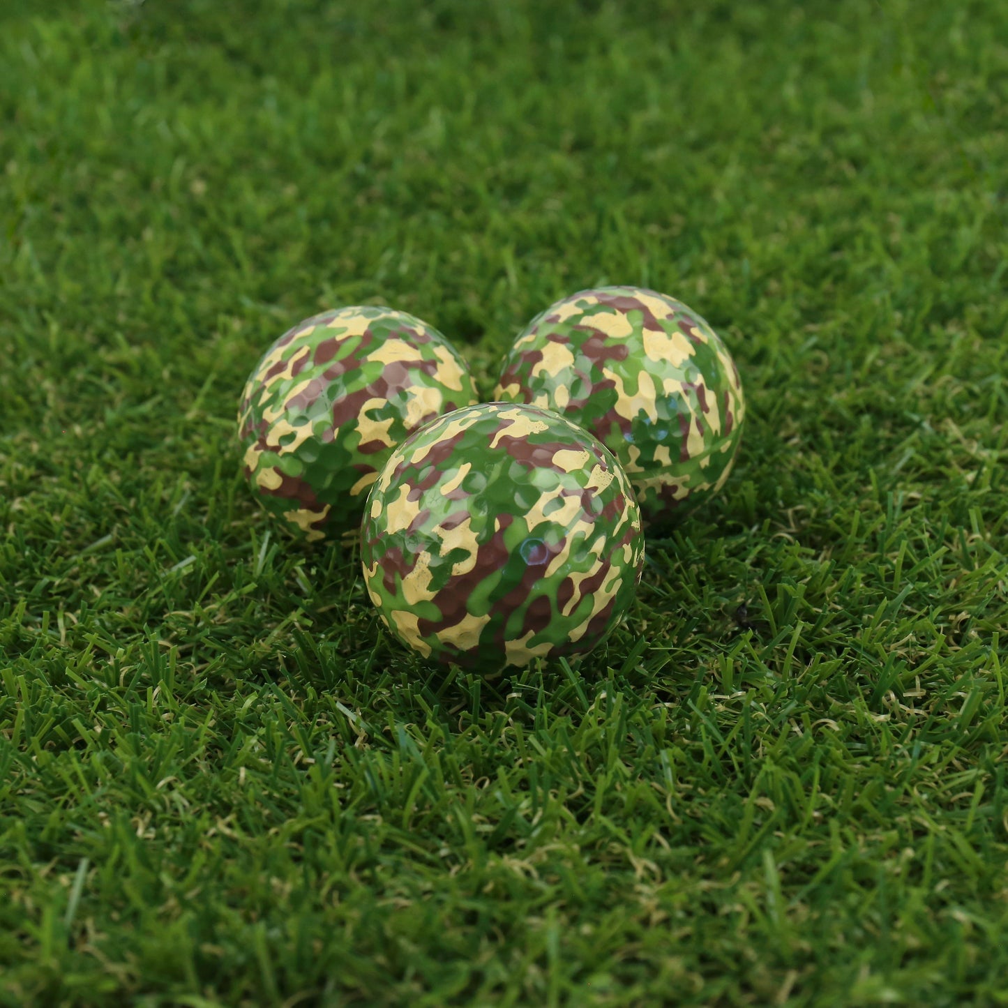 three of the camo golf balls displayed on the grass