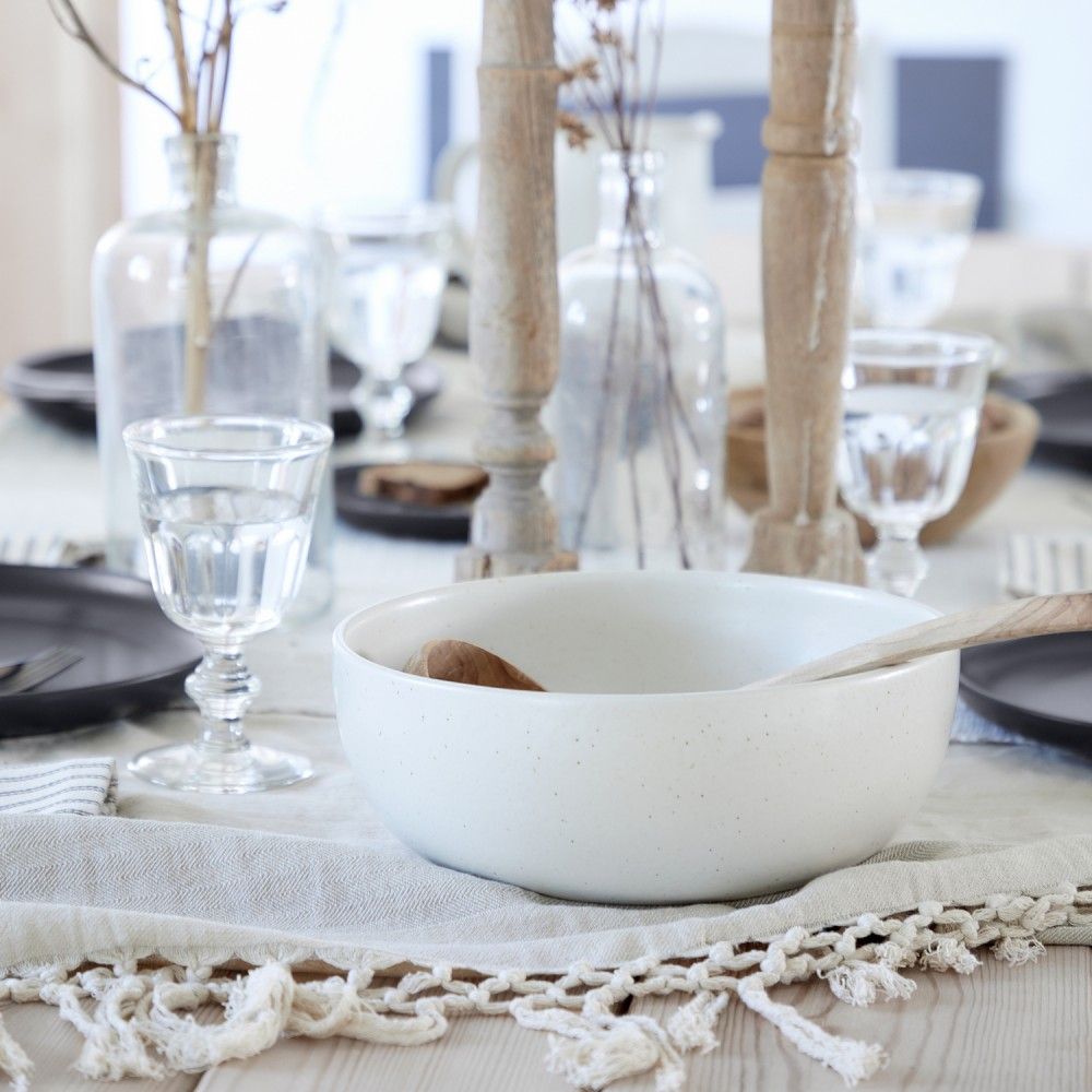 table setting with wood candlesticks, serving bowl, dinner plates, drinking glasses, vases with dried flowers on a oatmeal colored tablecloth
