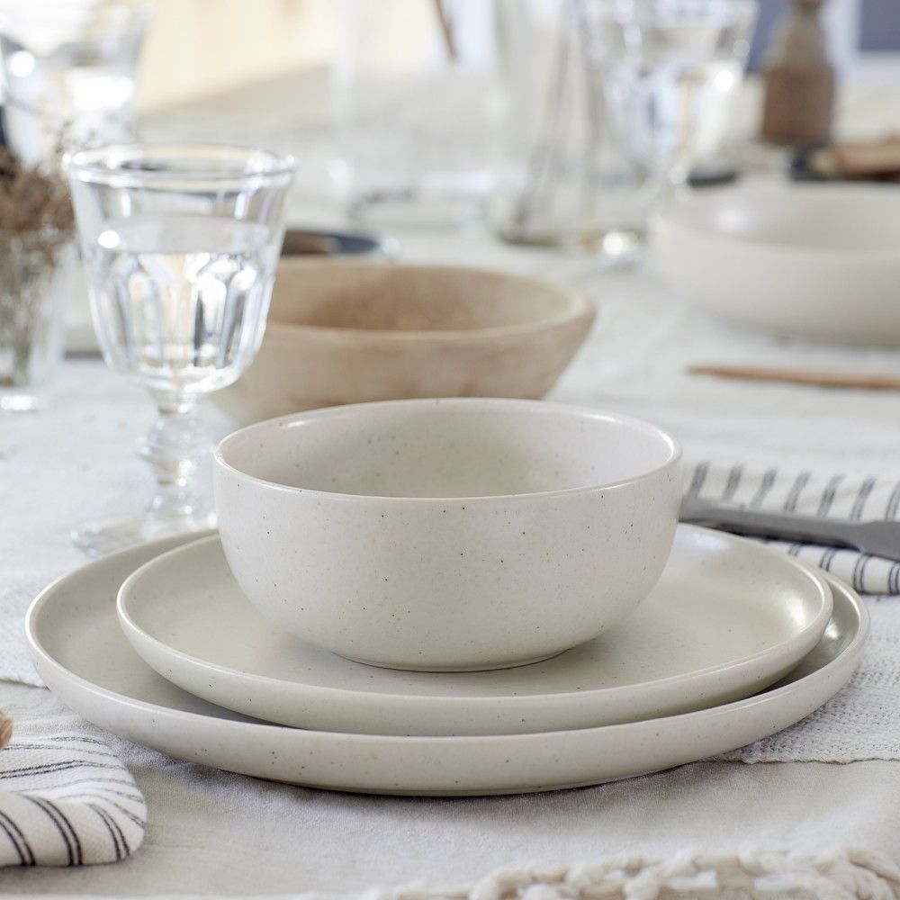 table setting with vanilla dinnerware, water filled glasses, napkins, and flatware on a white tablecloth