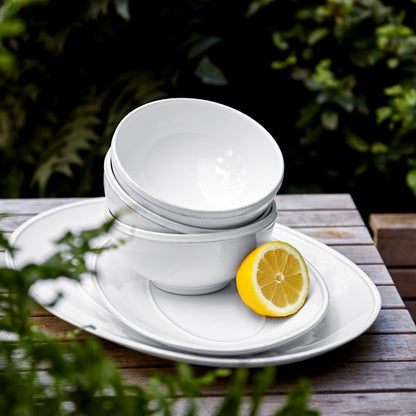 stack of white cereal bowls on an outdoor able surrounded by greenery.