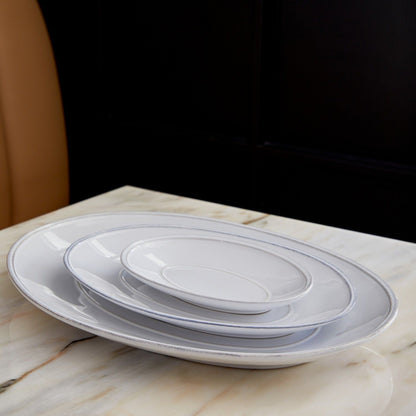 stack of 3 white oval platters on wooden table.