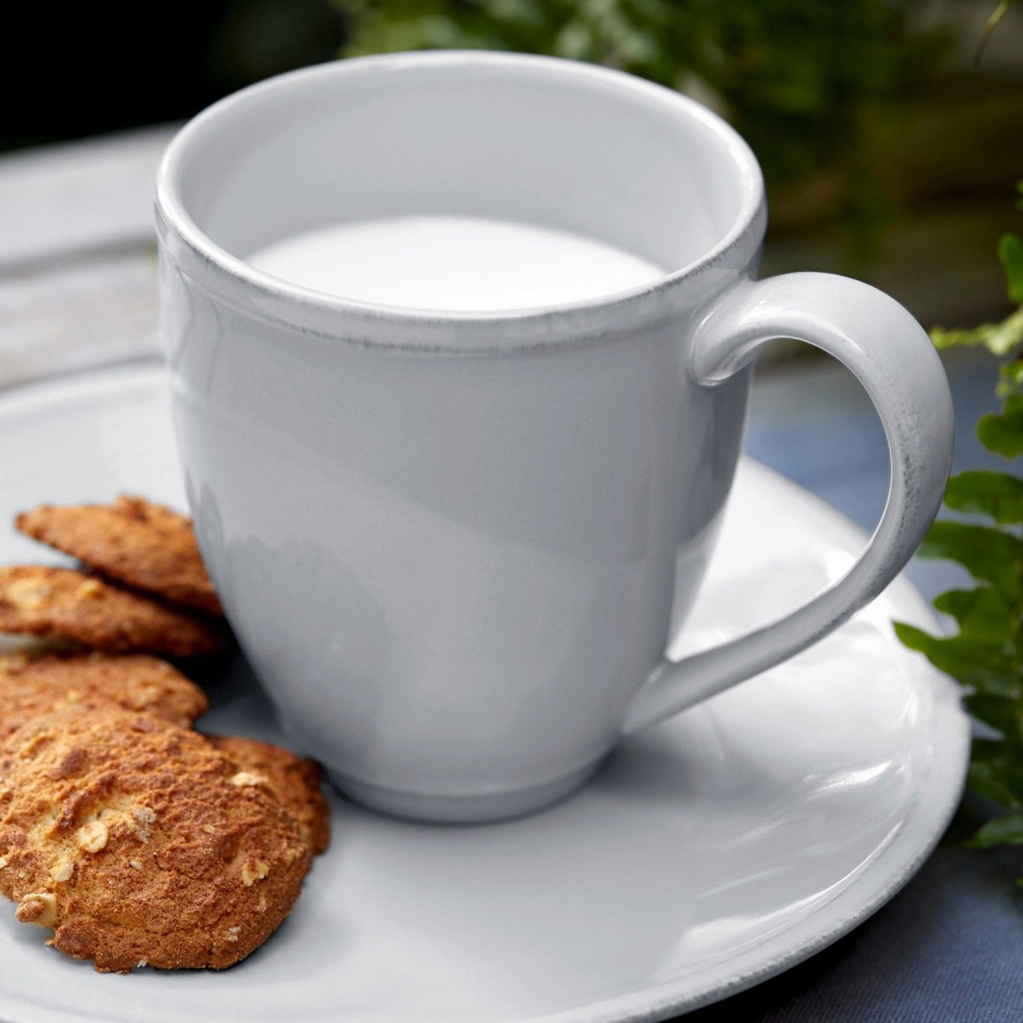 white mug filled with milk set on a white plate with cookies.