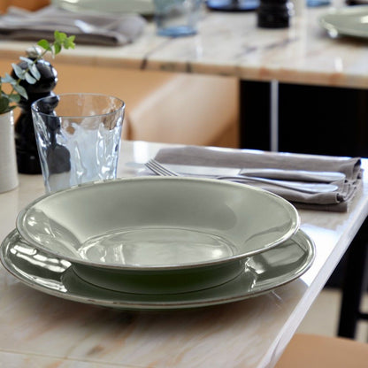 side view of a table setting of sage green dishes, silverware, and drinking glasses.