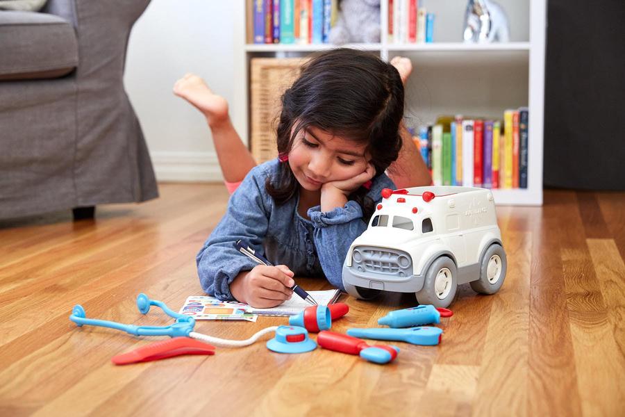 a young girl playing on the floor with the ambulance and doctors kit in a living room 