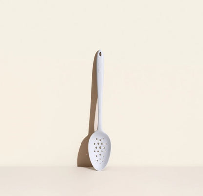 perforated spoon leaning against a cream colored background.