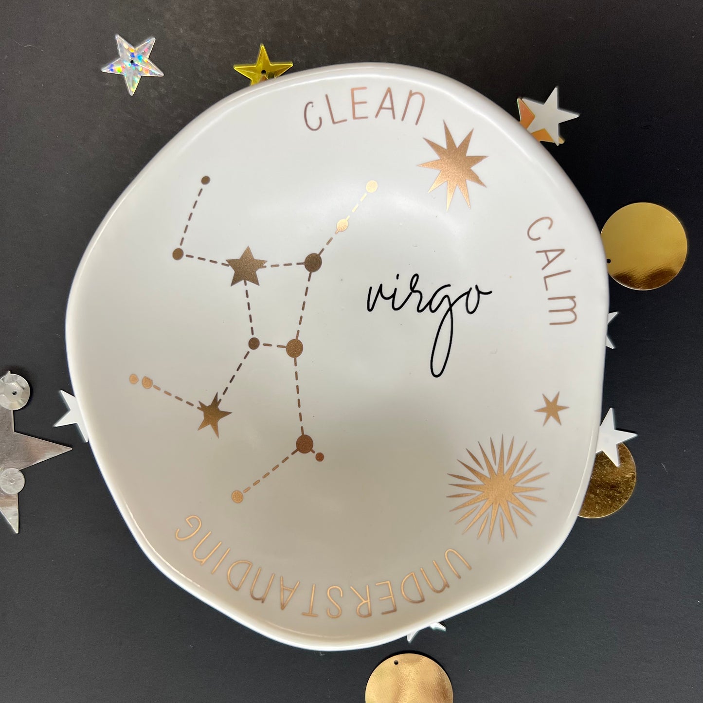 cream dish with gold stars and "Virgo Clean Calm Understanding" around the inner rim on a black background with scattered stars and orbs.