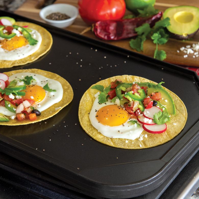 corn tortillas with eggs and veggies on griddle.