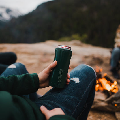 hopsulator slim can cooler held by a man sitting by a campfire