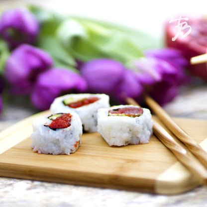 wood board with sushi and chop sticks on it with flowers in the background.