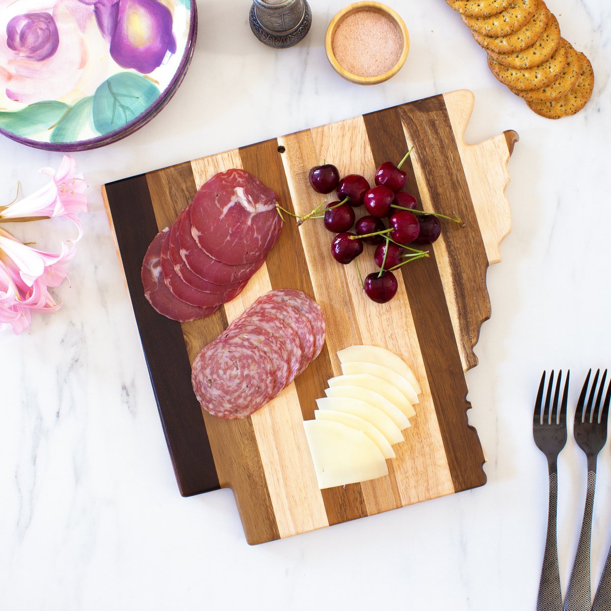 Arkansas shaped board with meat, cheese, and cherries on marble countertop.