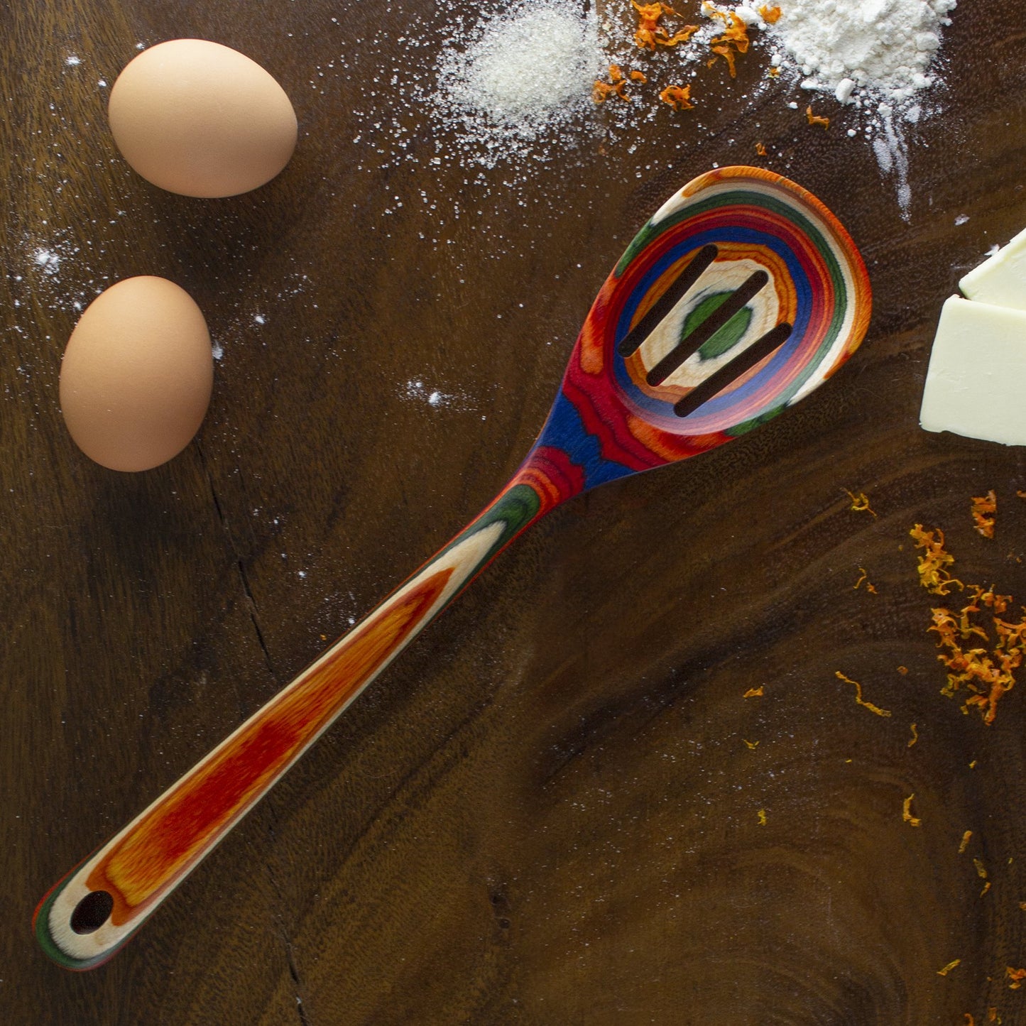 colorful spoon, eggs, and flour on wooden countertop.
