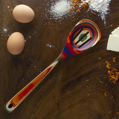 colorful spoon, eggs, and flour on wooden countertop.