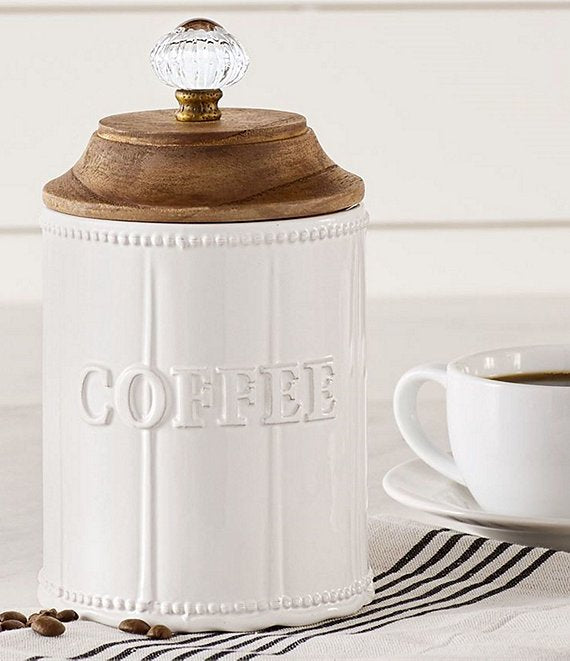 door knob coffee canister displayed in a kitchen next to a hand towel and coffee cup and saucer against a white background