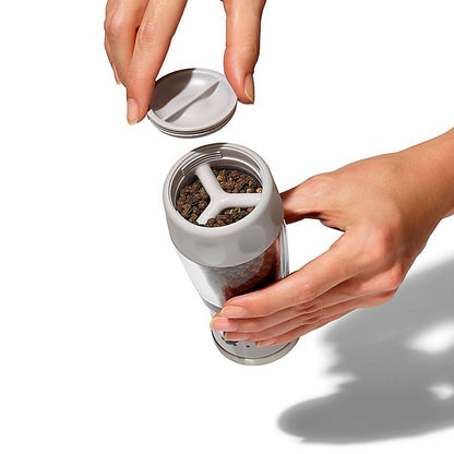 hands holding pepper grinder with base open for filling.