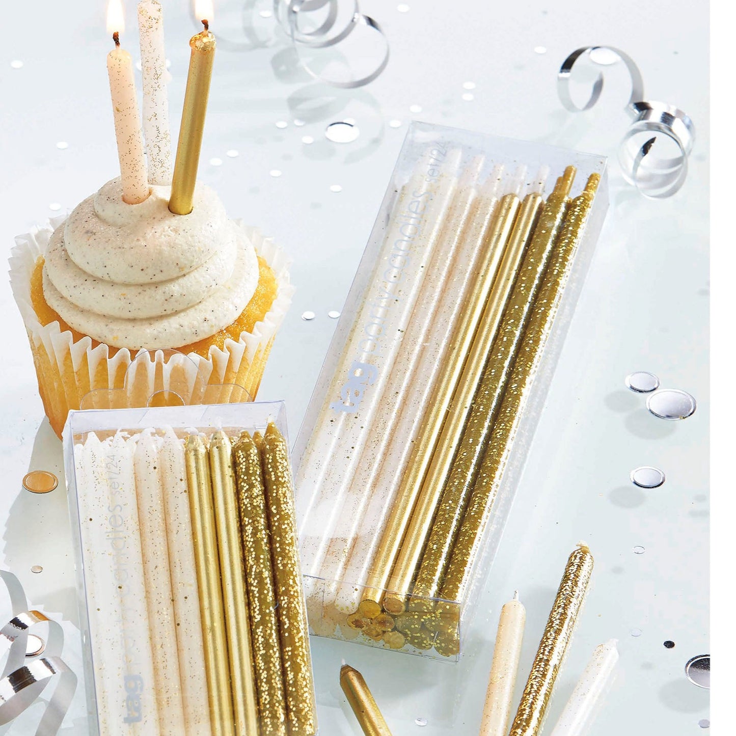 packages of gold and white glittered candles, cupcake with candles in it, and confetti and tabletop.