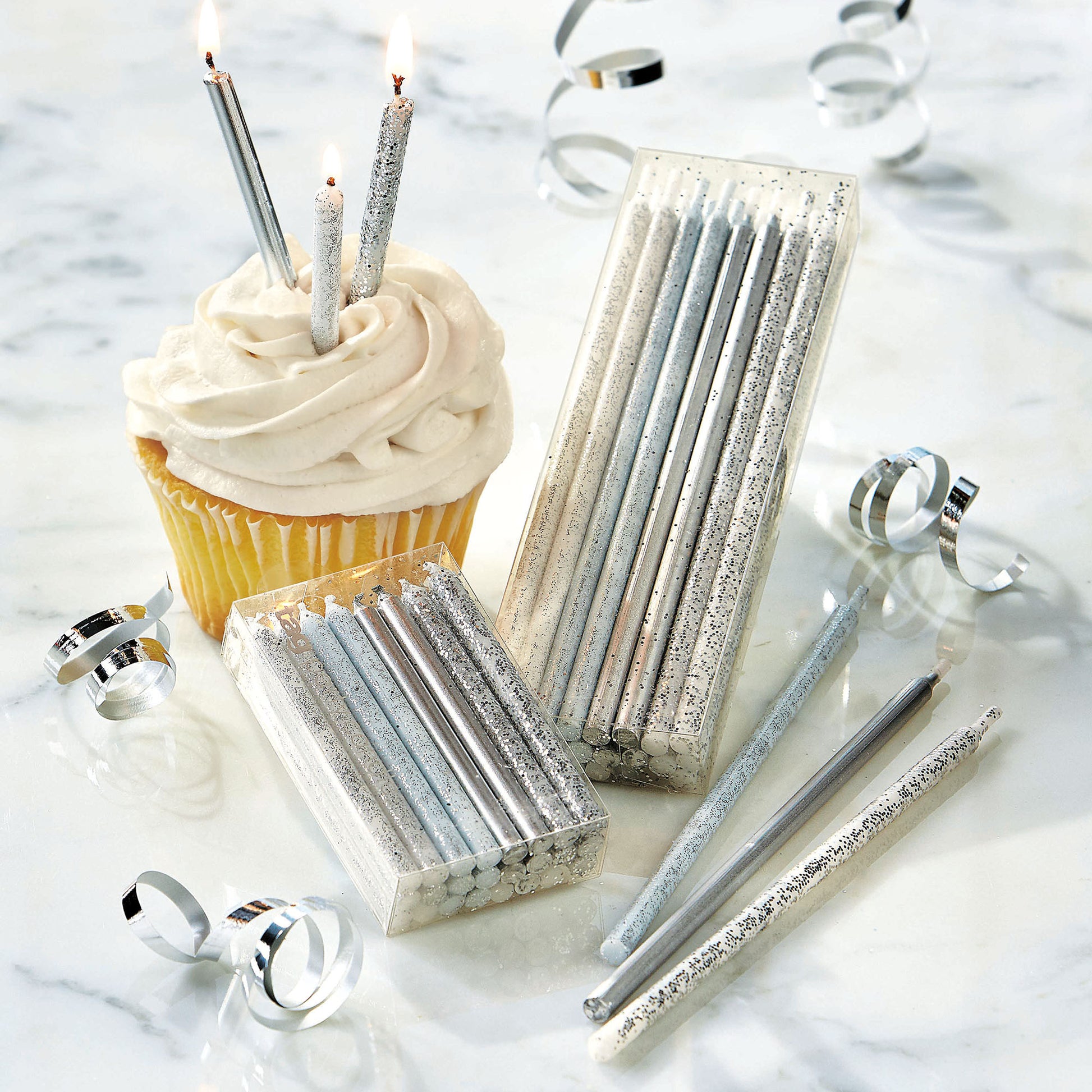 packages of silver and glittered candle, cupcake with candles in it, and confetti on table.