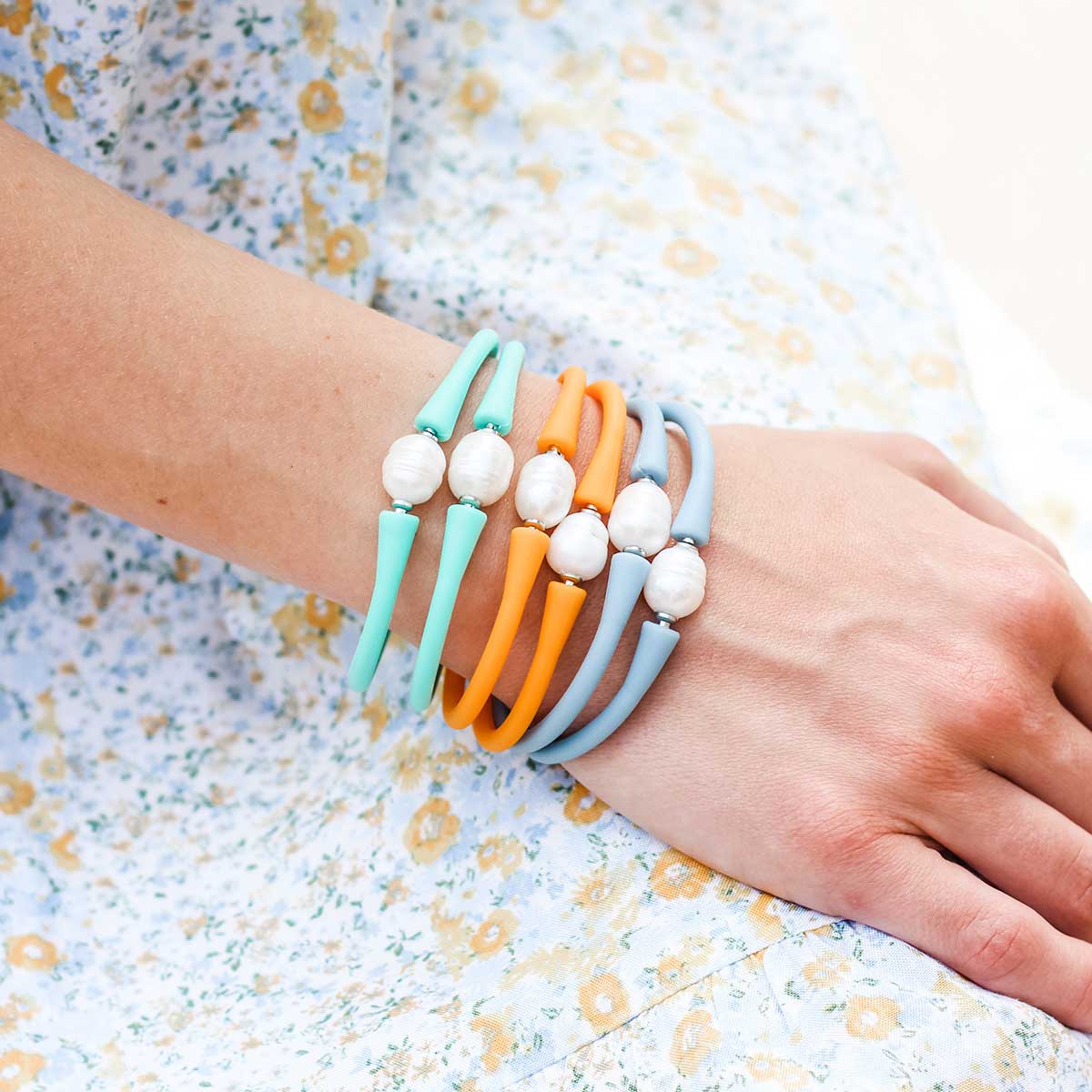 close up view of a woman wearing multiple bali freshwater pearl silicone bracelets against a floral dress