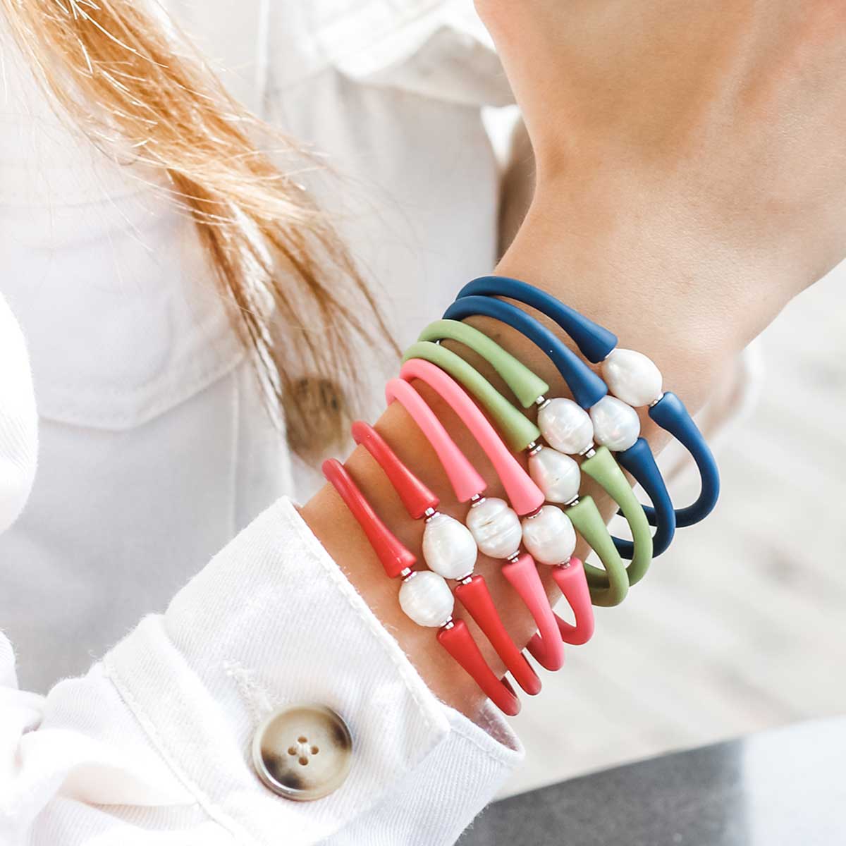 a woman wearing multiple bali freshwater pearl silicone bracelets against a white top