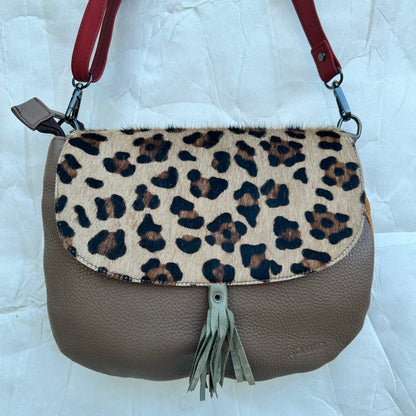 rounded taupe purse with cheetah print flap, taupe tassel, and red strap.