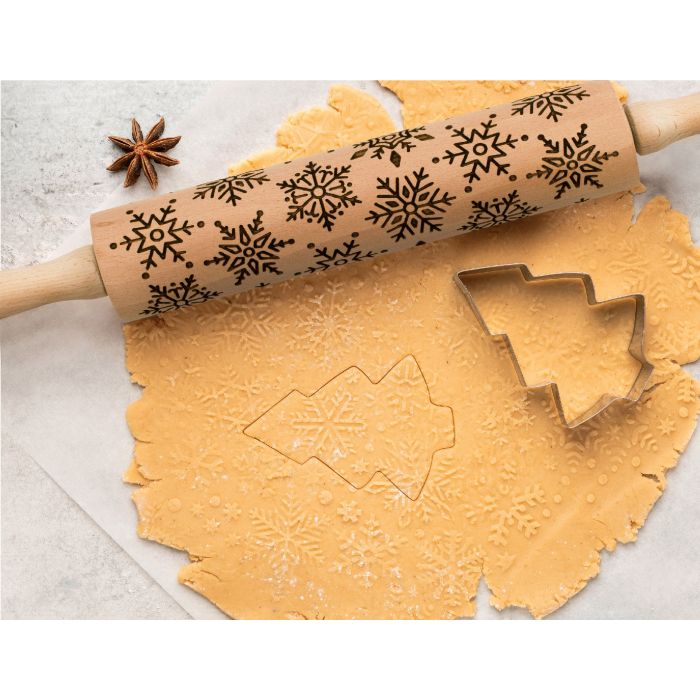 the snowflake design rolling pin displayed on rolled out cookie dough and cookie cutter on a white surface