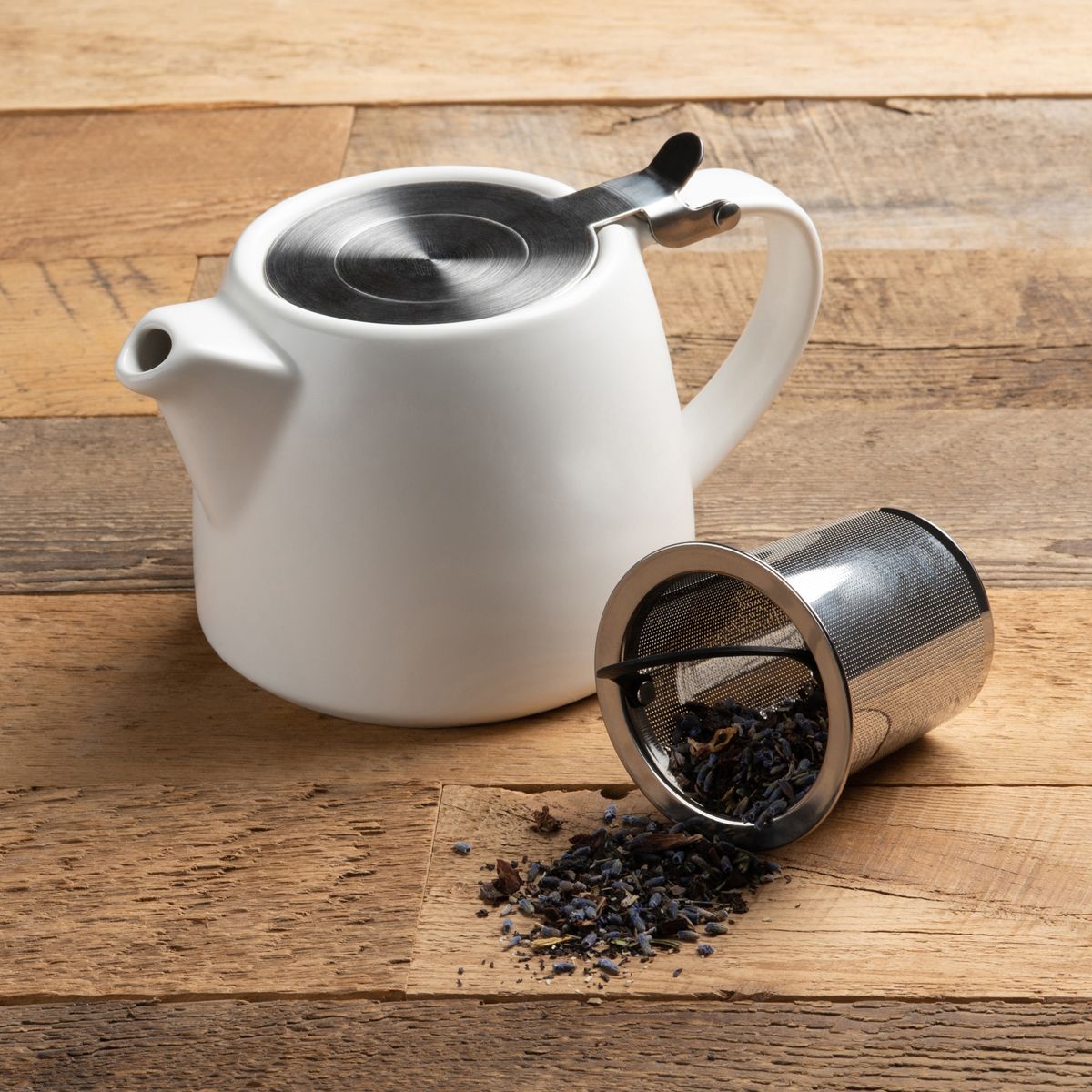 unity teapot displayed next to the metal infuser laying on its side with tea leaves spilling out on a rustic wood slat surface