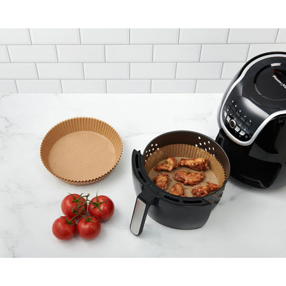 kitchen disposable air fryer liners displayed next to the air fryer basket that is sitting next to the air fryer on a white countertop