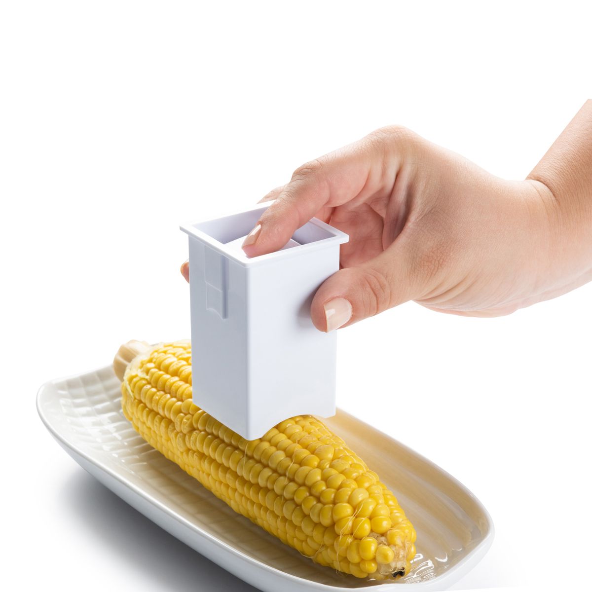 a persons hands demonstrating the use of the corn cob butterer on corn resting on a white plate
