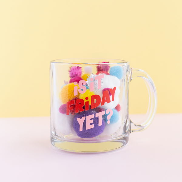 is it friday yet? glass mug filled with colorful poms on a yellow background.