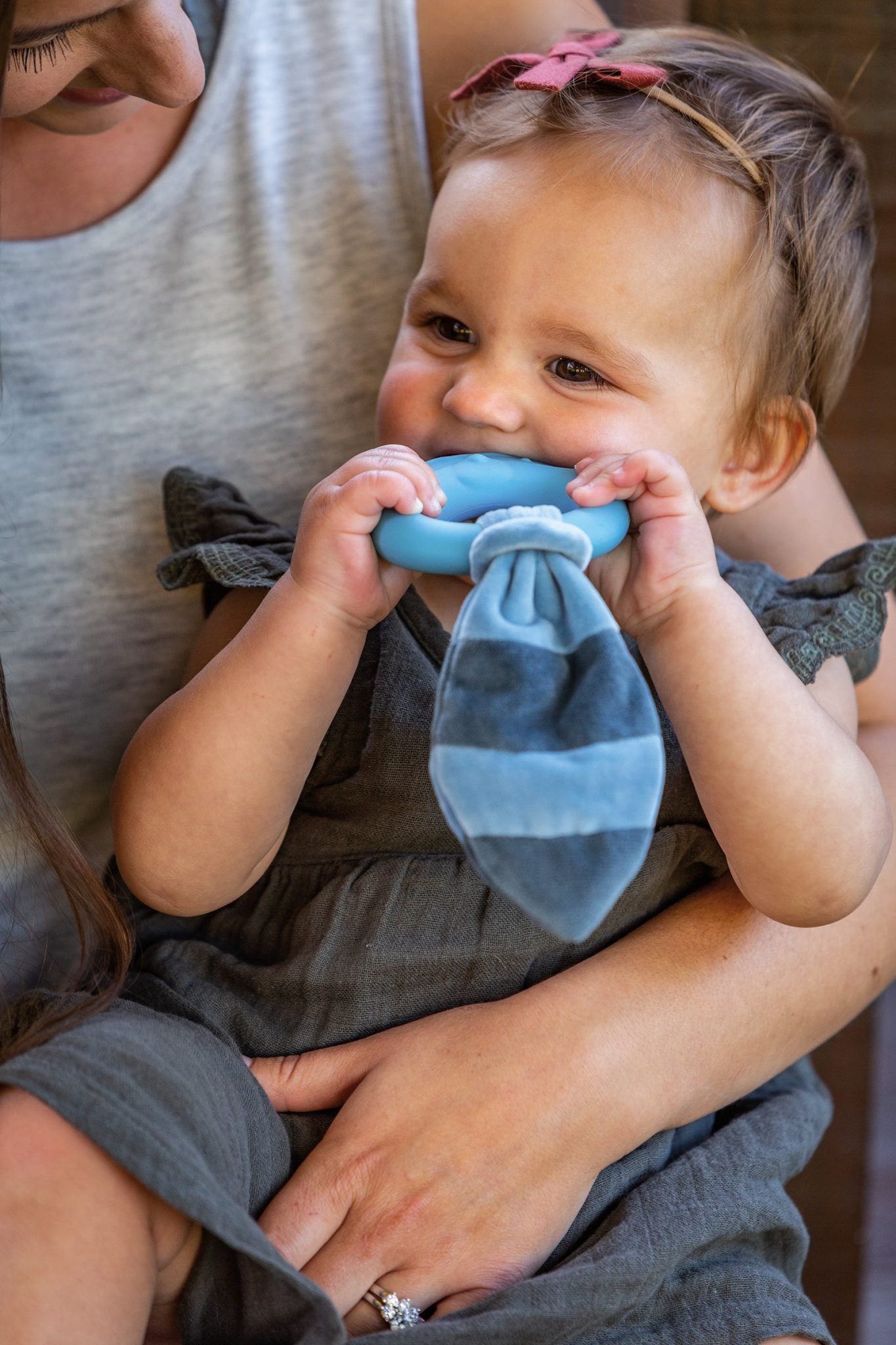 a woman holding a little girl while she chews on the leika little raccoon teether