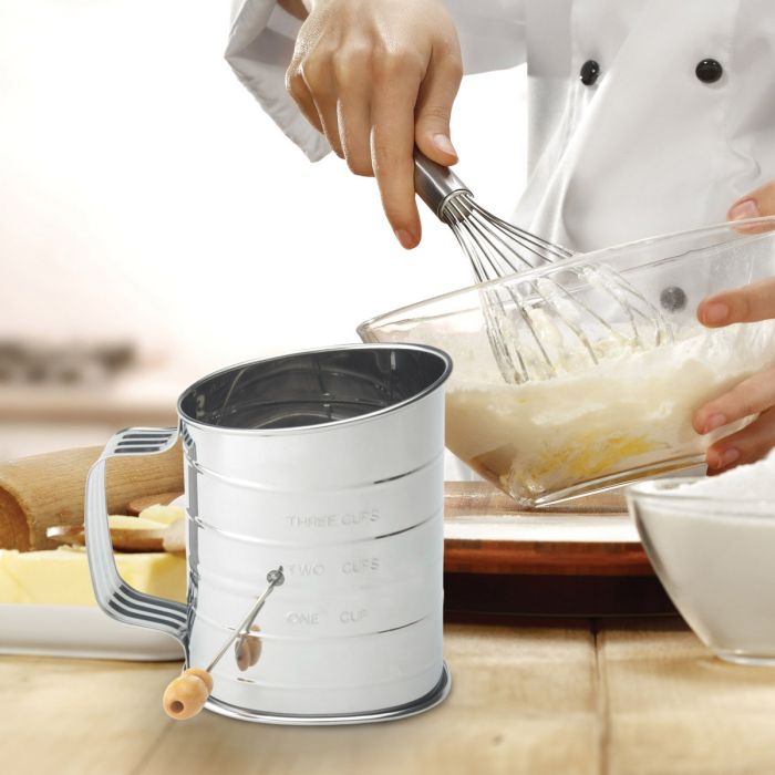 the hand crank stainless steel sifter displayed with a person baking in a kitchen