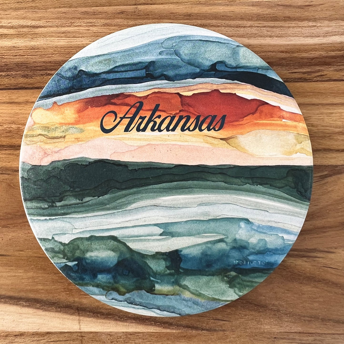 round coaster with abstract sunrise image and "Arkansas" printed in black across the top