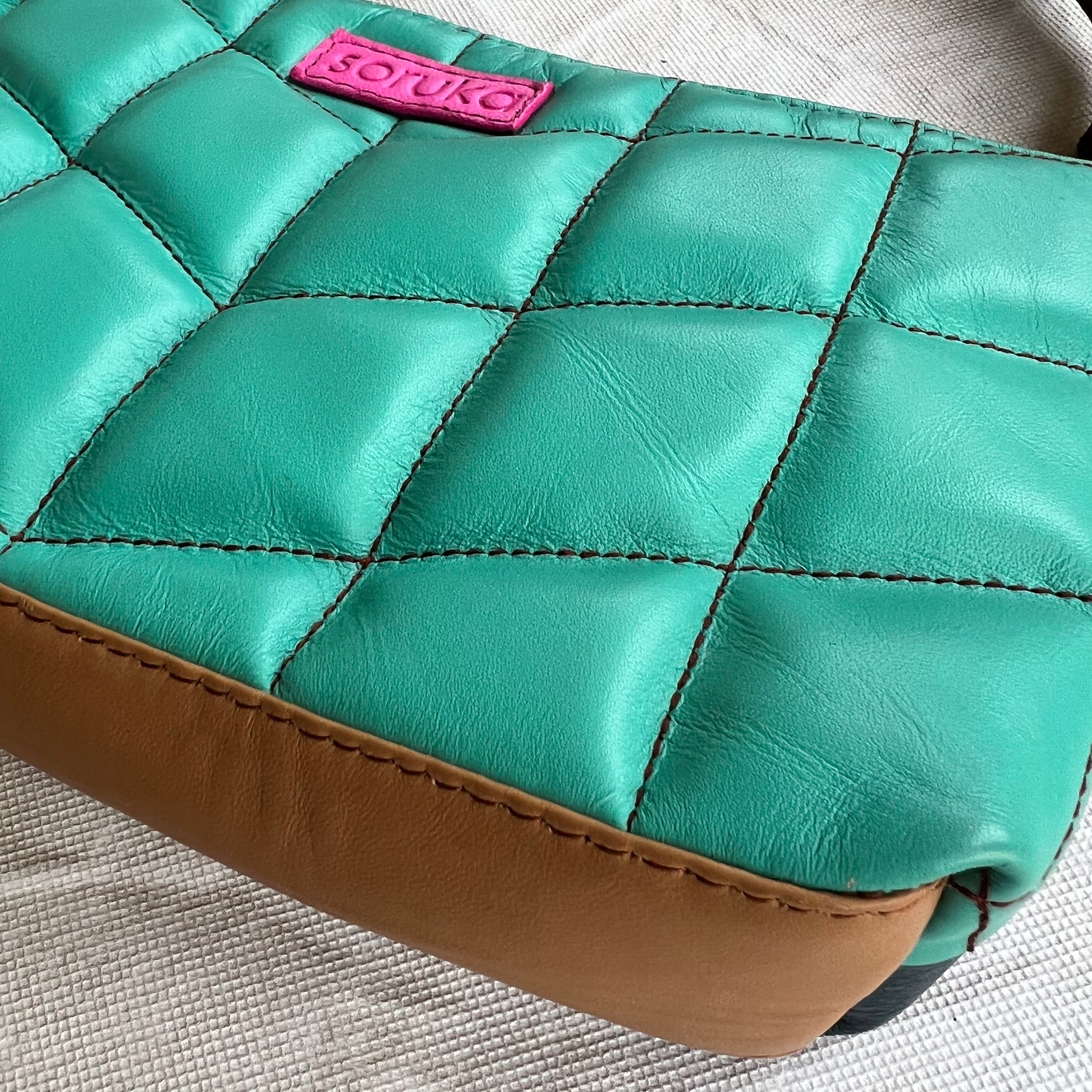 angled bottom view of seafoam green purse with brown base.