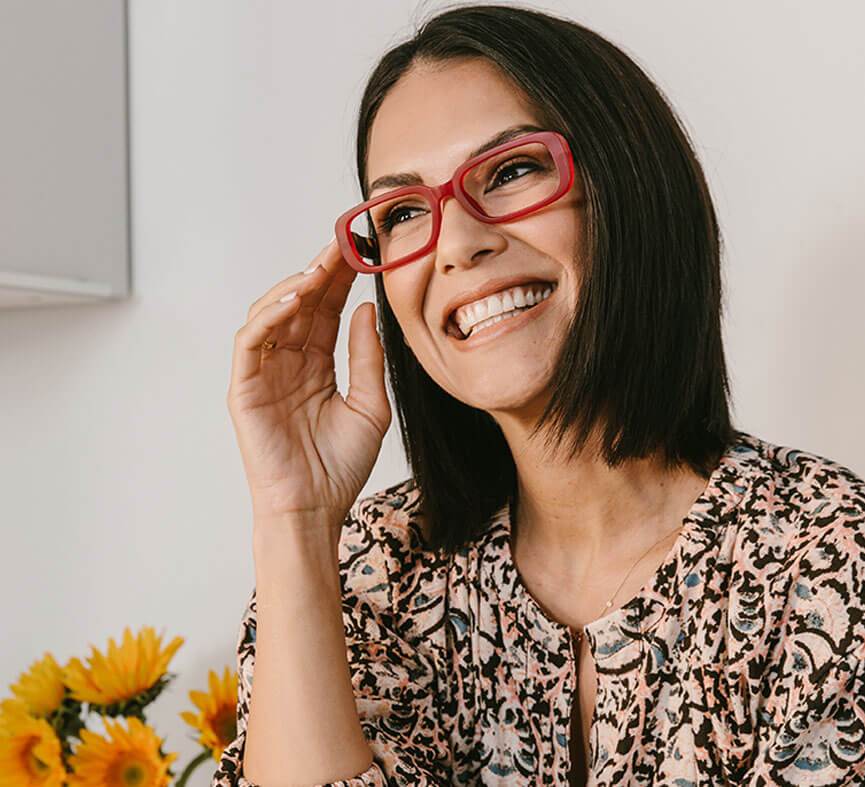 front view of a woman modeling the red willow glasses against a white background next to yellow flowers