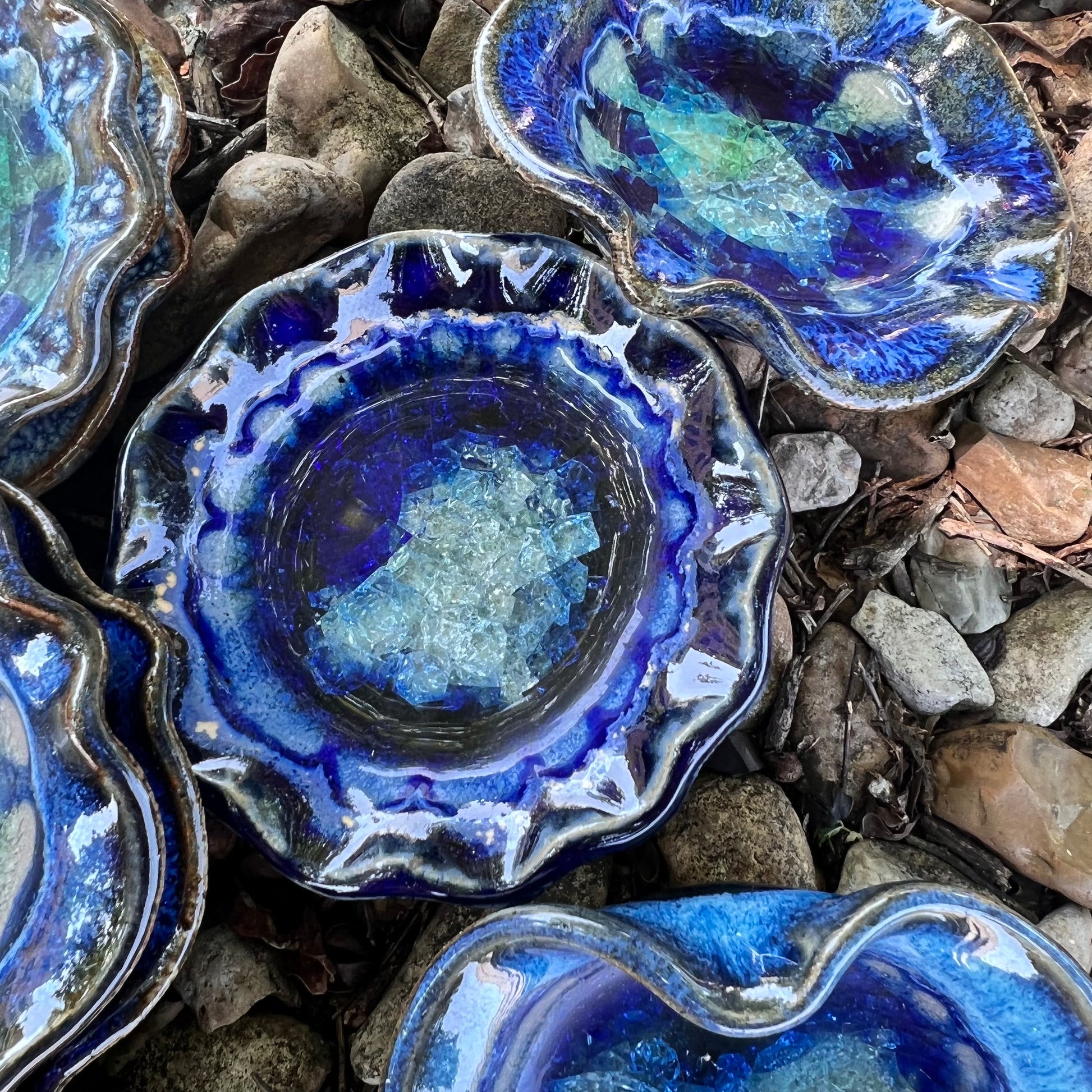 round beautiful blues crackled glass little dish displayed with more round and hearts on a bed of leaves ad rocks