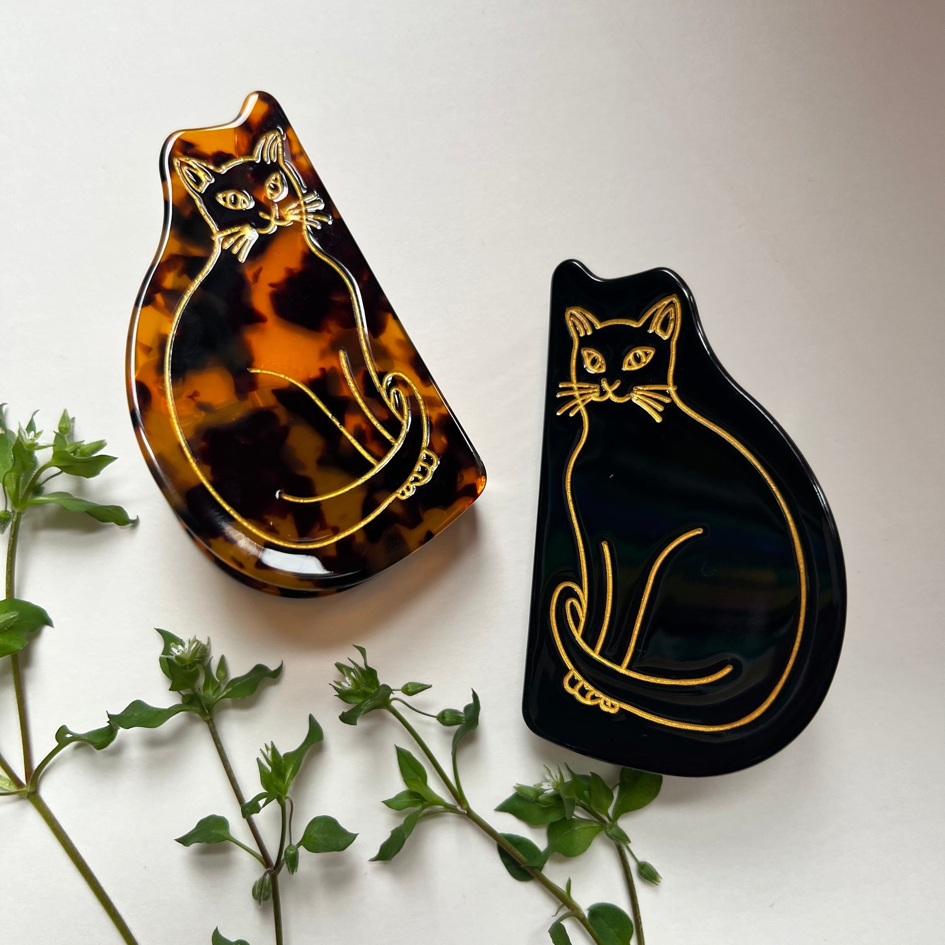 2 cat hair clips on a white background with greenery.