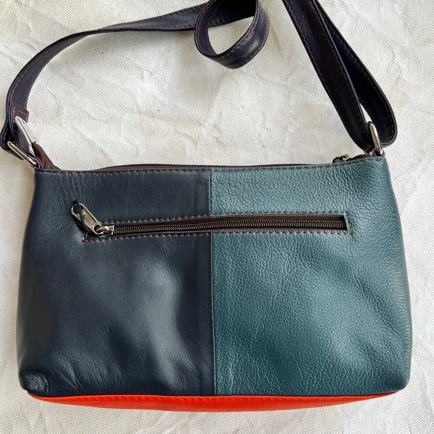 back view of purse that is half black, half blue  and has a zipper pocket.