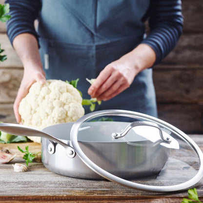 saute pan and lid in foreground with person holding cauliflower in background.