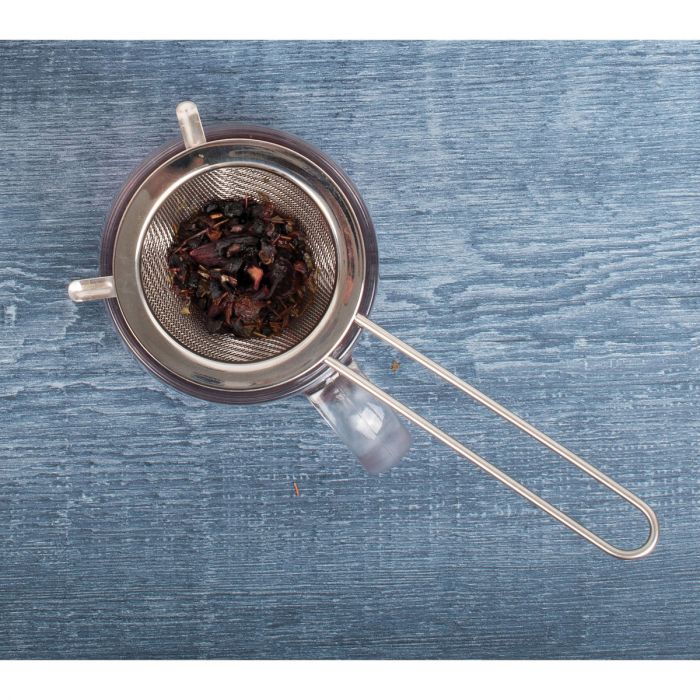 top view of the double ear conical tea strainer filled with tea leaves resting over a glass mug displayed on a gray wooden surface