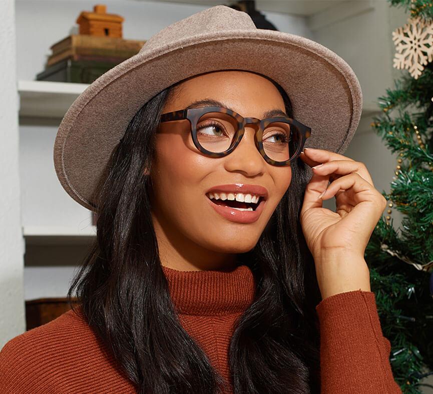 angled view of a woman modeling the tortoise stardust glasses while standing next to a christmas tree