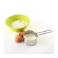 Stainless Steel Measuring Cup half filled with with flour and a bowl of flour and 2 eggs next to it.