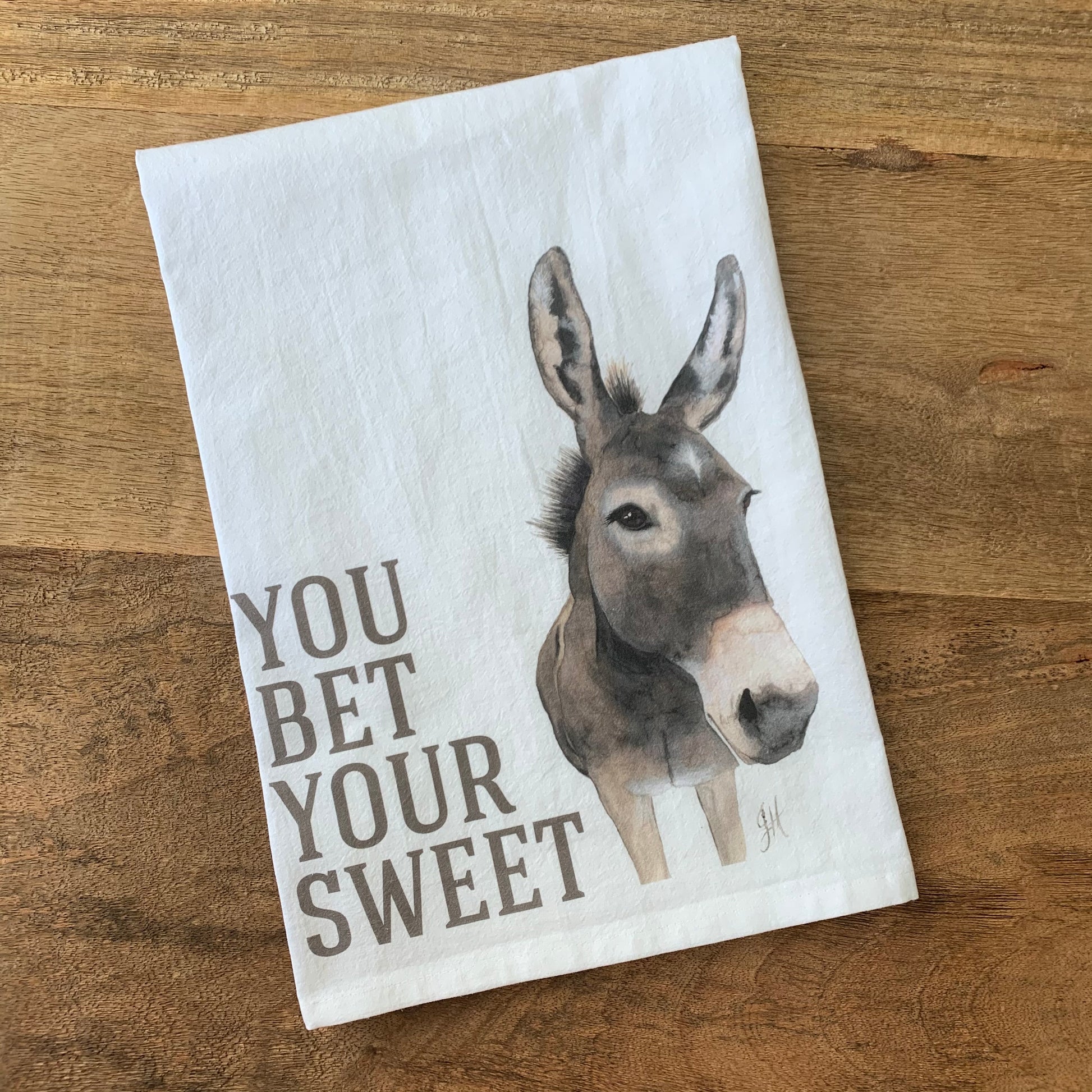 white flour sack towel with a painting of a donkey and text on a wood background