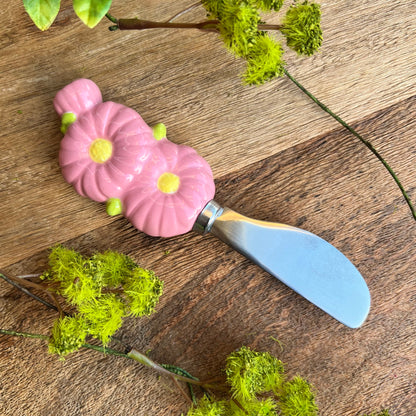 ceramic pink flower handle on stainless steel spreader on wooden background with sprigs of greenery.