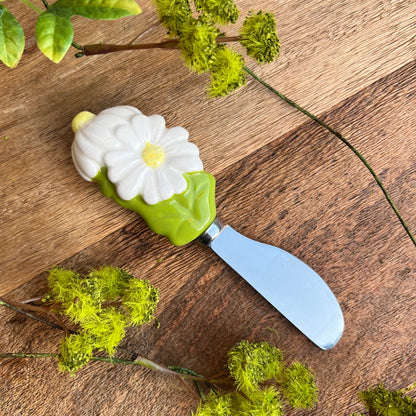 ceramic white flower handle on stainless steel spreader on wooden background with sprigs of greenery.
