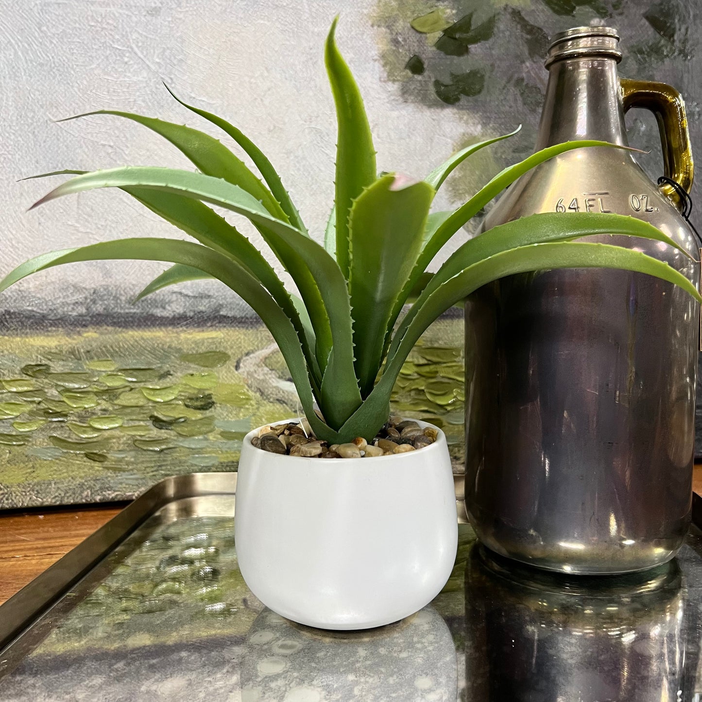 faux agave plant in white pot on a table next to a vase.
